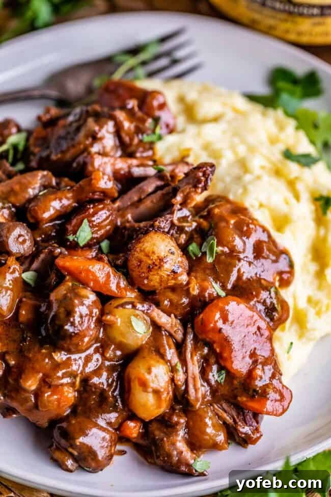 Classic French Beef Bourguignon 5 A plate featuring a serving of Beef Bourguignon stew nestled beside a dollop of creamy mashed potatoes, with a fork gently placed in the background, ready for a comforting meal.