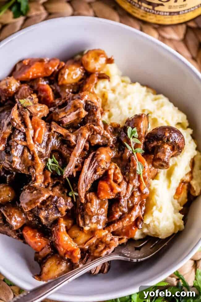 Classic French Beef Bourguignon 6 A close-up of a serving of Beef Bourguignon in a white bowl, accompanied by creamy mashed potatoes and a fork, highlighting its comforting and rustic appeal.
