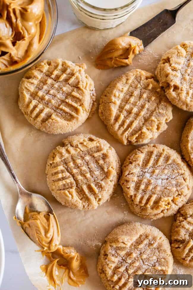 Melt-in-Your-Mouth Peanut Butter Cookies 12 Perfectly baked peanut butter cookies arranged on brown parchment paper, with a spoon of creamy peanut butter for garnish.