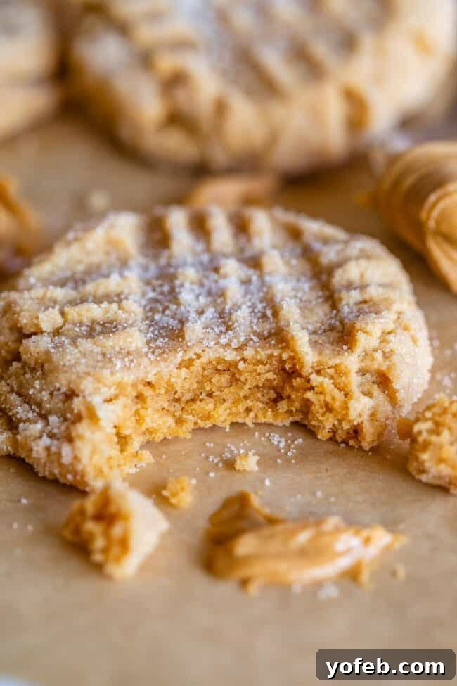 Melt-in-Your-Mouth Peanut Butter Cookies 3 Close-up of a soft peanut butter cookie with a bite taken out, resting on a baking tray next to a smear of peanut butter.