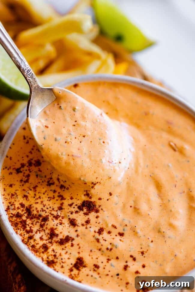 Whip Up Your Own Smoky Chipotle Sauce 14 A spoon lifting homemade chipotle mayo recipe from a small white bowl, lightly sprinkled with chipotle powder for garnish.