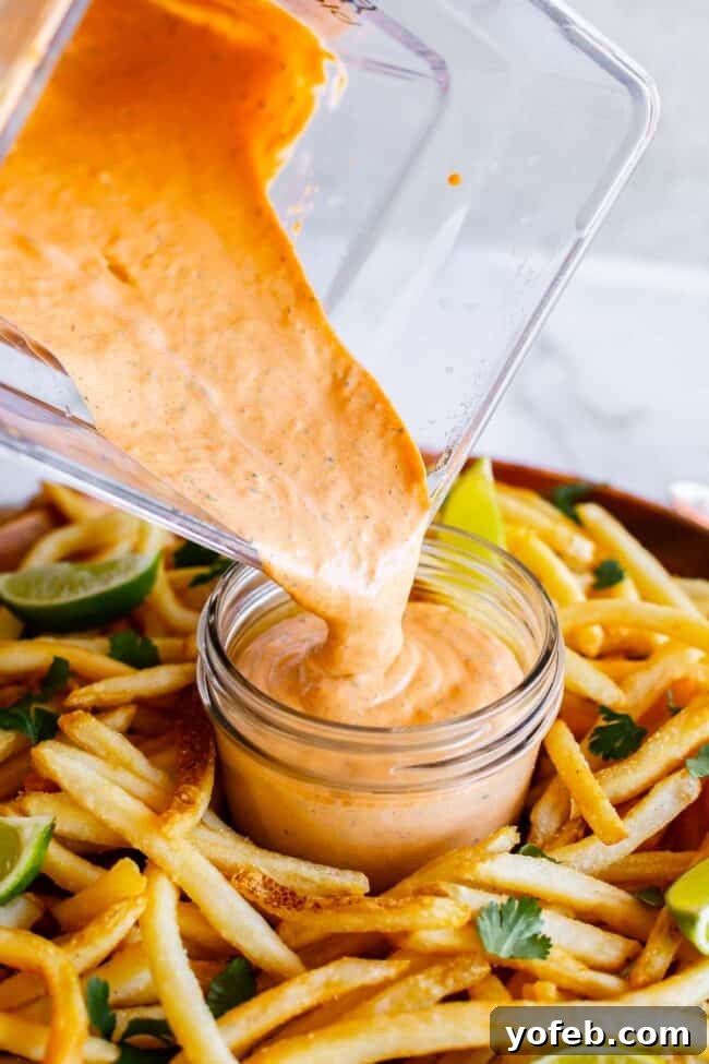 Whip Up Your Own Smoky Chipotle Sauce 8 Freshly blended chipotle mayo sauce being poured from a blender into a clear mason jar, surrounded by crispy french fries.
