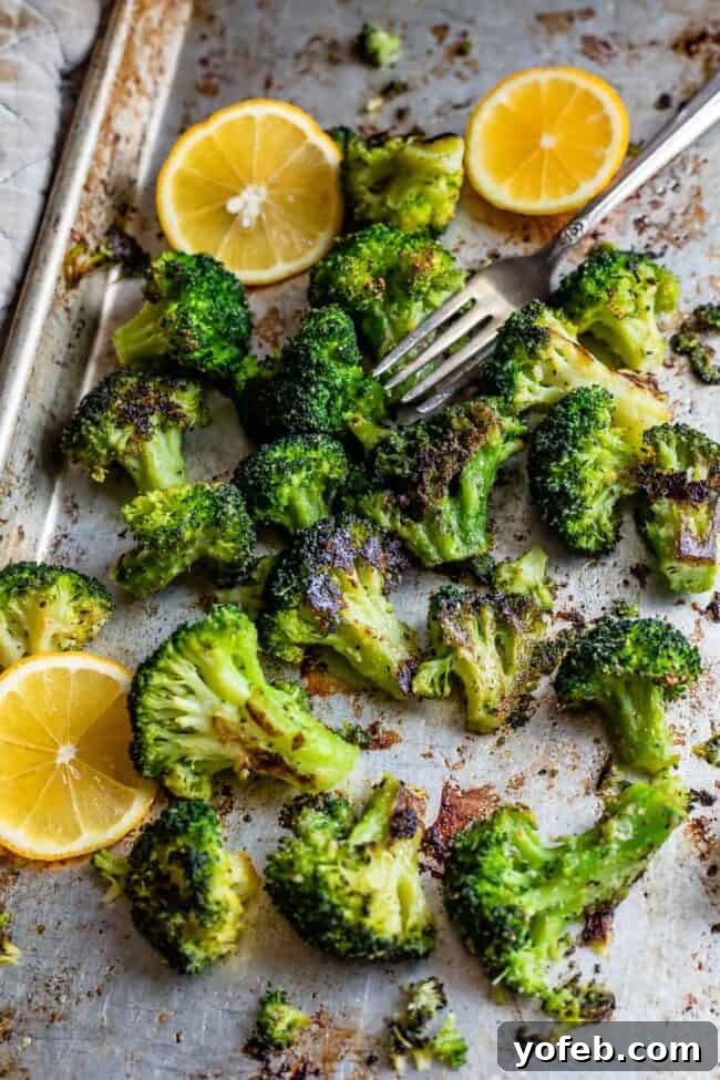 A close-up shot of oven-roasted broccoli florets on a sheet pan, garnished with fresh lemon slices and a fork, highlighting their appealing texture and readiness to serve.
