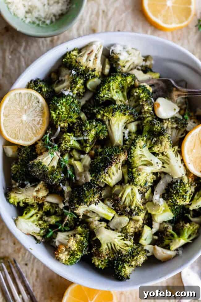 A white bowl filled with glistening, perfectly roasted broccoli, accented by fresh lemon slices on the side. The florets exhibit appealing charred edges, promising a delightful flavor and texture.