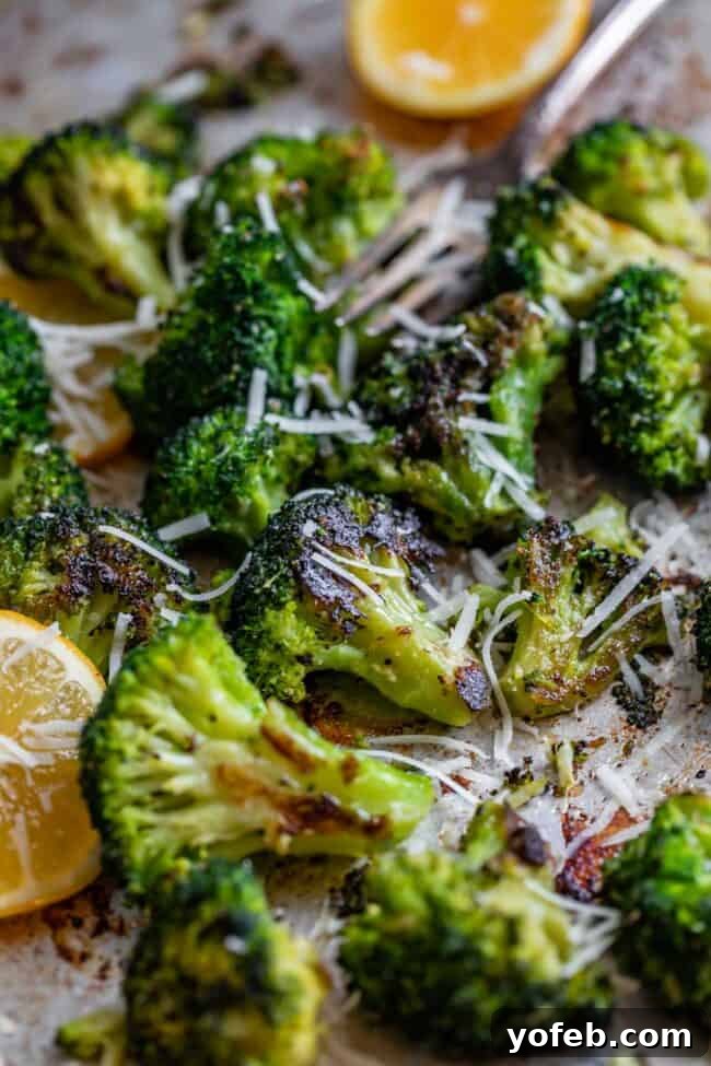 Crispy oven-roasted broccoli florets seasoned with garlic and a sprinkle of Parmesan cheese, accompanied by fresh lemon wedges and a fork, creating an appetizing and healthy presentation.
