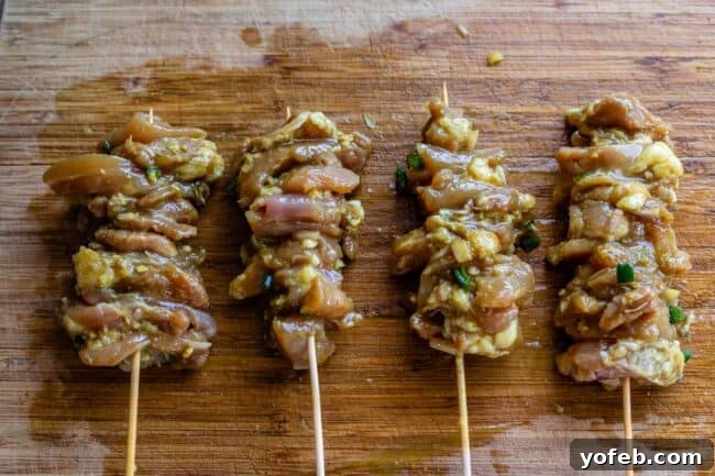 Authentic Thai Chicken Satay with Creamy Peanut Sauce 12 Marinated chicken pieces, tightly threaded onto wooden skewers, arranged on a wooden cutting board, ready for grilling.