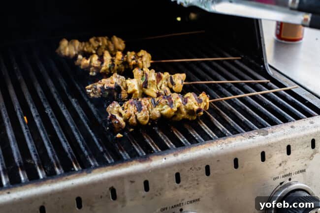 Authentic Thai Chicken Satay with Creamy Peanut Sauce 13 Marinated chicken thighs on wooden skewers cooking on a hot grill, with visible grill marks forming.