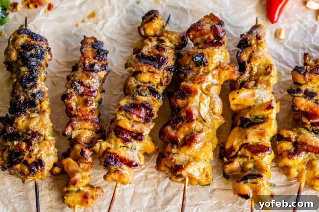 Authentic Thai Chicken Satay with Creamy Peanut Sauce 14 A perfectly arranged row of grilled, marinated chicken thighs on wooden skewers, showcasing their golden-brown color and juicy appearance.
