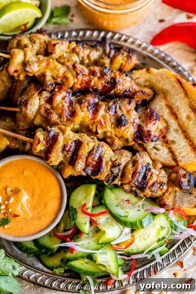 Authentic Thai Chicken Satay with Creamy Peanut Sauce 16 A beautifully composed shot of grilled Thai Chicken Satay, with a bowl of peanut sauce, fresh cucumber salad, and grilled bread on the side.