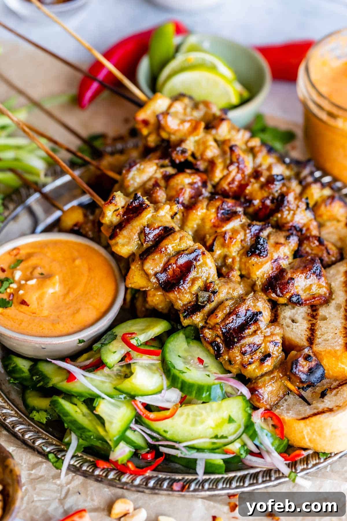 Authentic Thai Chicken Satay with Creamy Peanut Sauce 3 Close-up of a bowl of creamy Thai peanut sauce, garnished with herbs, next to a silver platter of chicken satay and fresh cucumber salad.