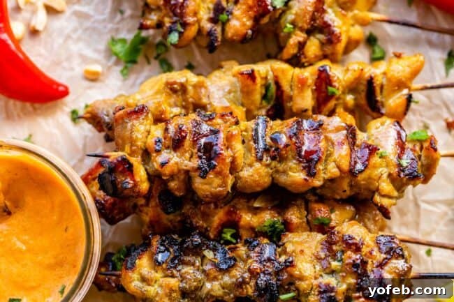 Authentic Thai Chicken Satay with Creamy Peanut Sauce 5 A row of beautifully grilled Thai Chicken Satay skewers resting on a silver platter, with a bowl of rich peanut sauce beside them.