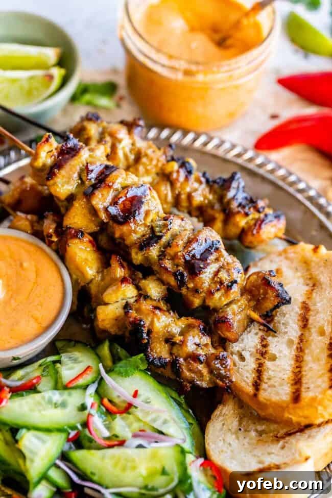 Authentic Thai Chicken Satay with Creamy Peanut Sauce 8 A vibrant platter featuring grilled Thai Chicken Satay skewers, slices of toasted bread, a bowl of refreshing cucumber salad, and a generous serving of peanut sauce.