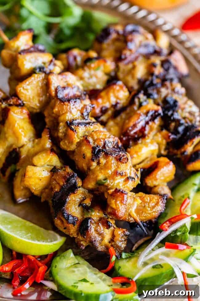 Authentic Thai Chicken Satay with Creamy Peanut Sauce 9 A silver platter presents perfectly cooked chicken satay with a side of fresh Thai cucumber salad, ready to be enjoyed.