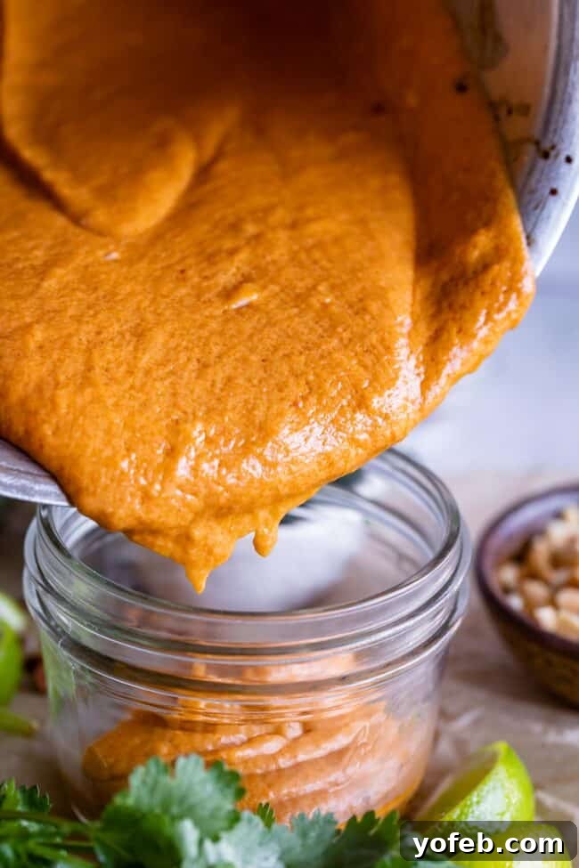 Effortless Homemade Peanut Sauce 12 A step-by-step image showing how to make Thai peanut sauce, with a hand pouring the freshly made, smooth sauce into a glass jar for storage or serving.