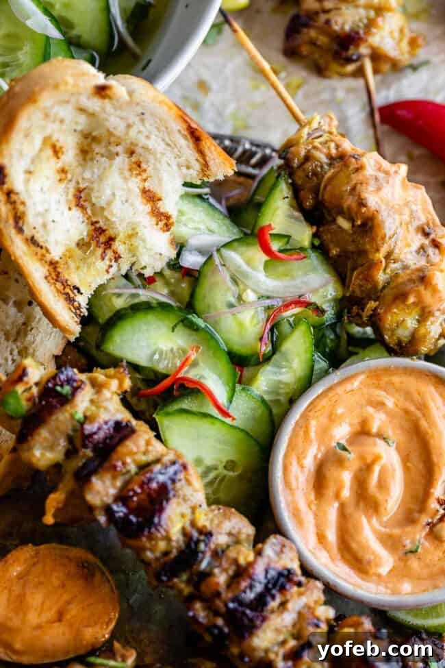 Effortless Homemade Peanut Sauce 13 A beautifully arranged plate featuring Thai-inspired chicken satay skewers, a small bowl of creamy peanut sauce, a fresh Thai cucumber salad, and slices of grilled bread, creating a harmonious and delicious meal.