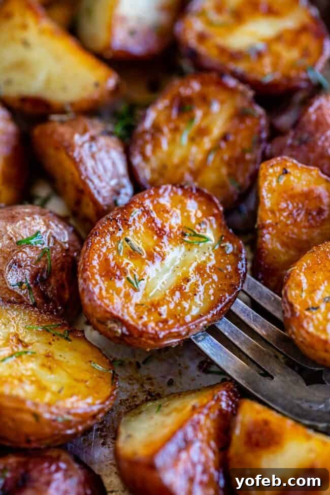 Crispy Oven-Roasted Red Potatoes 14 close-up of roasted baby red potatoes on a baking sheet, garnished with herbs, one potato pierced with a fork to check doneness