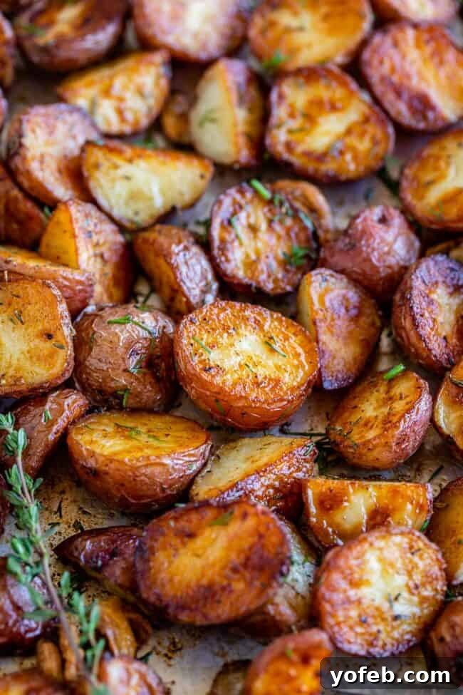 Crispy Oven-Roasted Red Potatoes 4 crispy roasted red potato pieces with fresh thyme on a large baking sheet, ready to be served