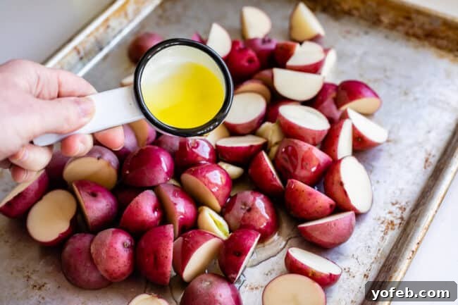 Crispy Oven-Roasted Red Potatoes 8 pouring olive oil over chopped red potatoes on a baking sheet, ensuring each piece is coated for roasting