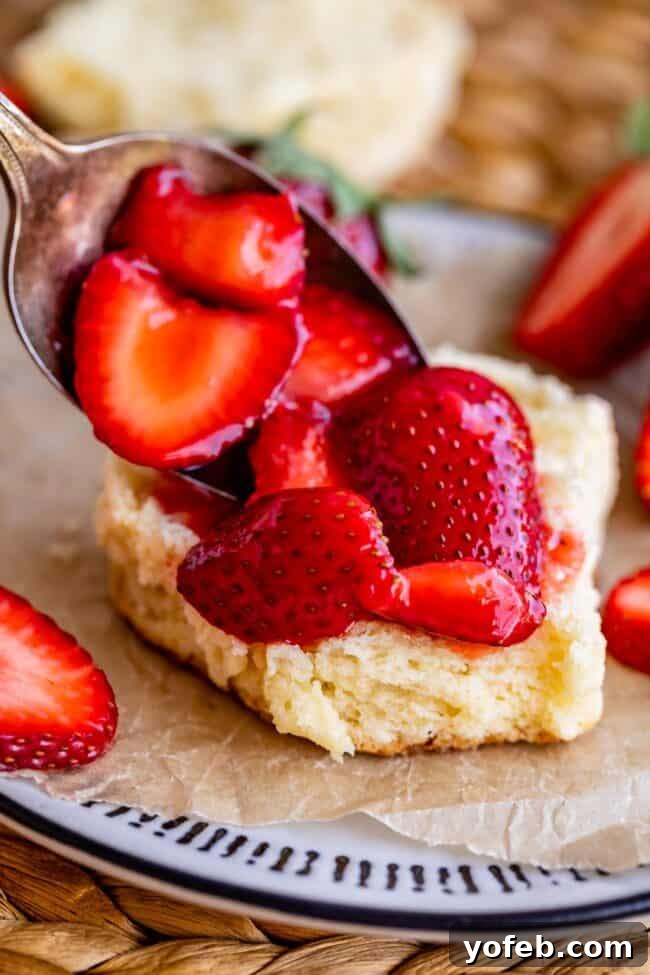 Spoonfuls of luscious strawberries being placed onto a shortcake on a plate.