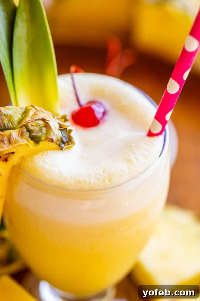 Island Oasis Piña Colada 11 A frothy virgin piña colada in a goblet, adorned with a polka dot straw, a fresh pineapple wedge, and a maraschino cherry, with delightful drips cascading down the side of the glass.