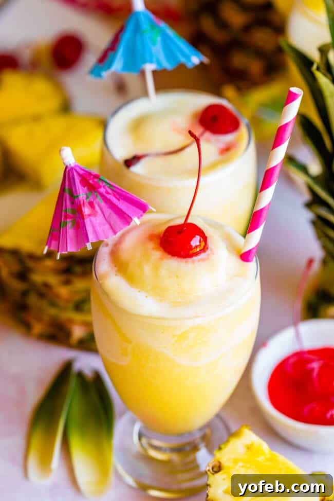 Island Oasis Piña Colada 3 Two enticing virgin piña coladas, each adorned with a bright maraschino cherry, a festive straw, and a small umbrella, evoking a sense of tropical relaxation.
