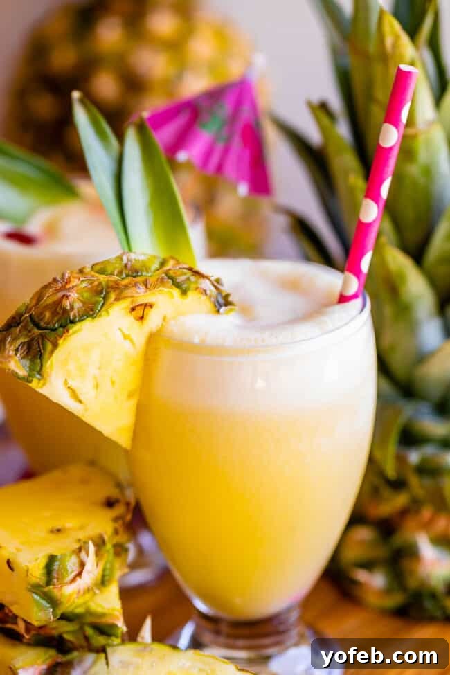 Island Oasis Piña Colada 6 A refreshing virgin piña colada in a clear glass, complete with a pineapple wedge and a straw, promising a cool and delicious sip.