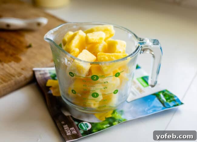 Island Oasis Piña Colada 7 Approximately 10 ounces of frozen pineapple chunks, neatly arranged in a clear glass measuring cup, ready for blending.