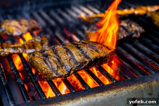 Mastering Carne Asada 16 outside skirt steak on a grill with flames in the background.
