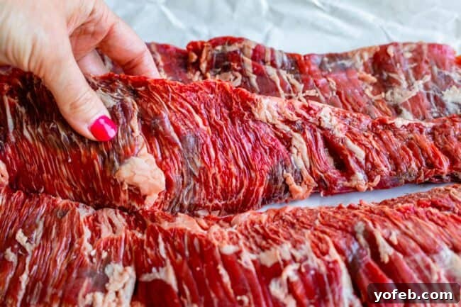 Mastering Carne Asada 9 a long strip of raw outside skirt steak held with a hand.
