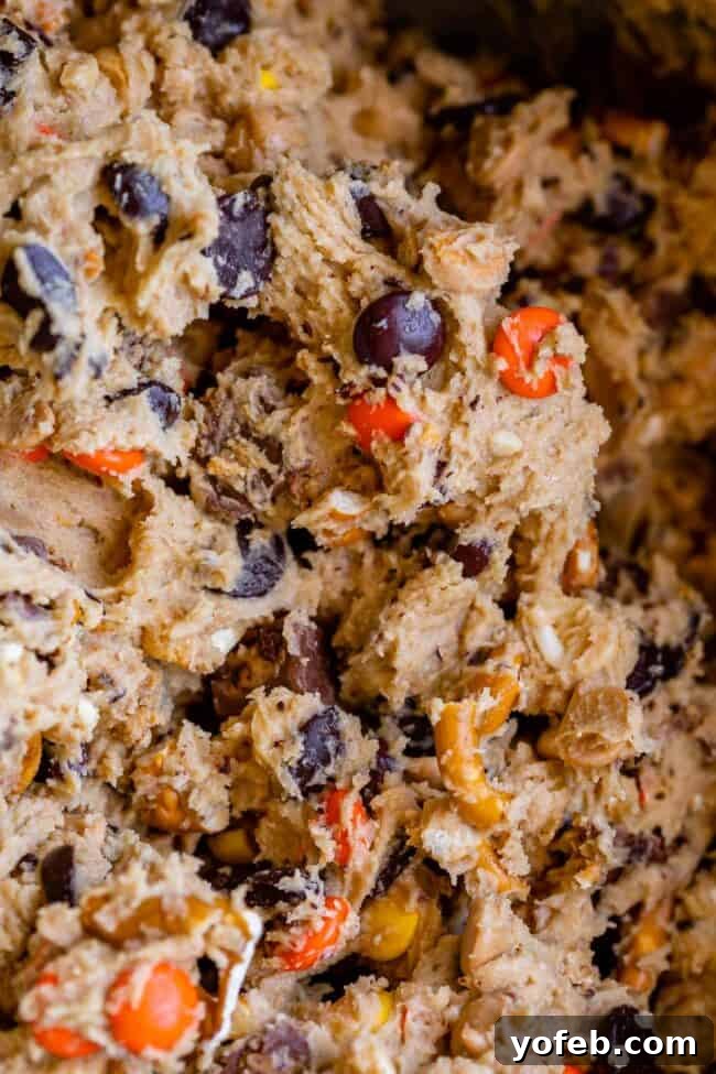 Loaded Reese's Peanut Butter Pretzel Cookies 12 Raw peanut butter cookie dough in a mixing bowl, generously filled with Reese's Pieces, pretzels, peanut butter chips, and chocolate chips.