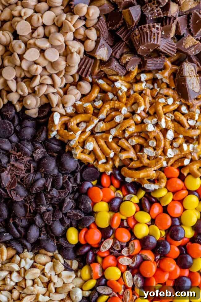 Loaded Reese's Peanut Butter Pretzel Cookies 6 An array of cookie ingredients laid out on a wooden board: peanut butter chips, dark chocolate chips, pretzels, Reese's Pieces, and quartered Reese's Peanut Butter Cups.