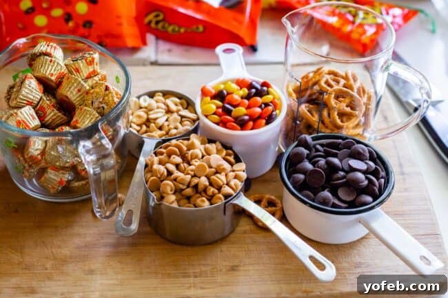 Loaded Reese's Peanut Butter Pretzel Cookies 10 Various mix-in ingredients for Reese's cookies in measuring cups on a wooden cutting board, including Reese's cups, peanuts, peanut butter chips, Reese's Pieces, and chocolate chips.