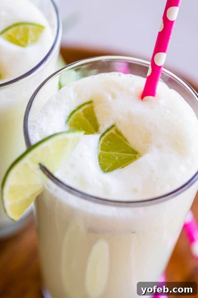 Creamy Brazilian Lemonade Recipe 5 A glass of Brazilian Limeade, bright with lime wedges and a pink straw, showcasing its tempting frothy top.