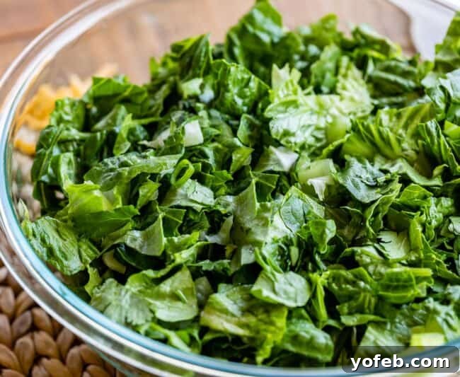 Crisp, chopped romaine lettuce and vibrant green onions tossed together in a large clear glass bowl, forming the fresh base of a Cobb salad.