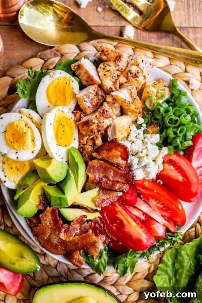 A vibrant, fully dressed Cobb salad with meticulously arranged rows of chicken, bacon, cheese, eggs, and fresh vegetables, ready to be enjoyed.
