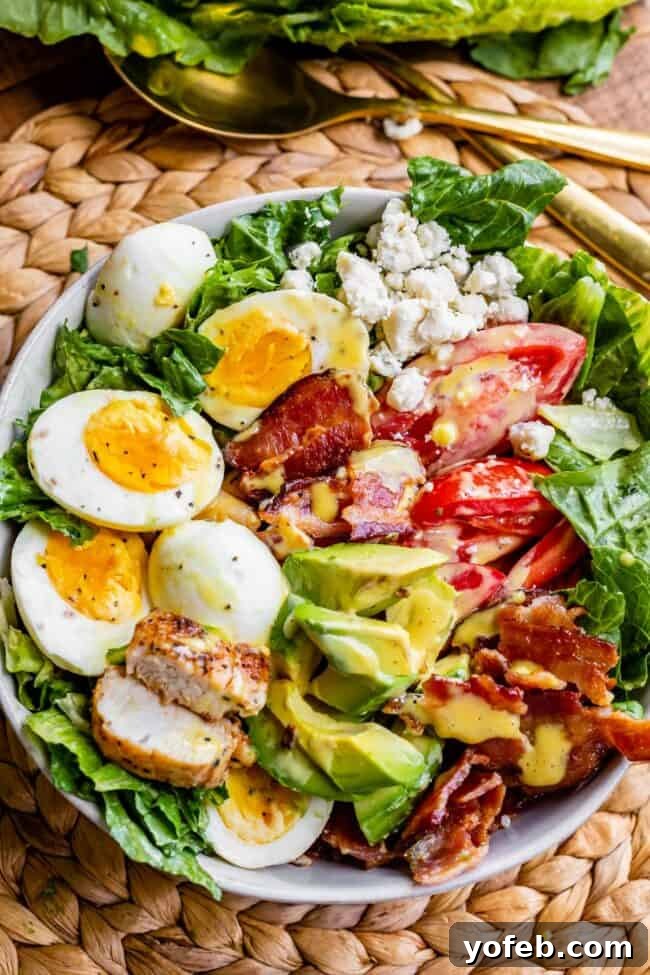 A vibrant, hearty Cobb salad served in a deep bowl with a golden serving spoon, highlighting the generous mix of fresh and savory ingredients.