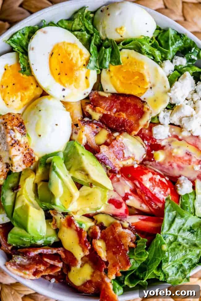 A classic Cobb salad served in a elegant white bowl, generously drizzled with a creamy dressing, showcasing its rich layers of ingredients.