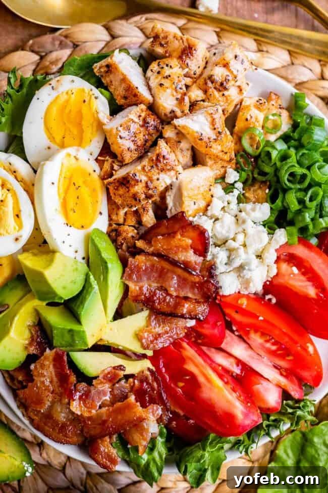 Close-up of a chicken Cobb salad on a rustic plate, featuring perfectly cooked eggs, crisp bacon, fresh tomatoes, crumbled cheese, and tender chicken pieces.