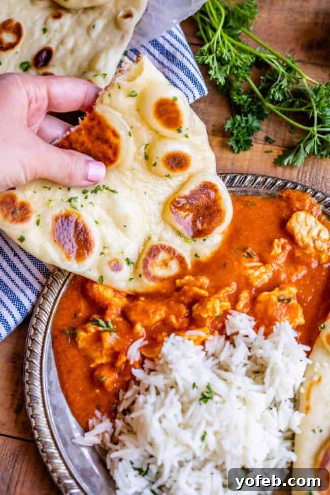 a hand dipping homemade naan into chicken curry next to white rice on a plate.