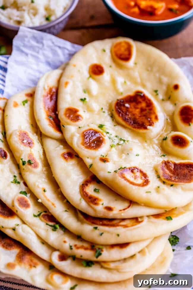several buttered naan breads on a piece of parchment paper, sprinkled with fresh parsley.