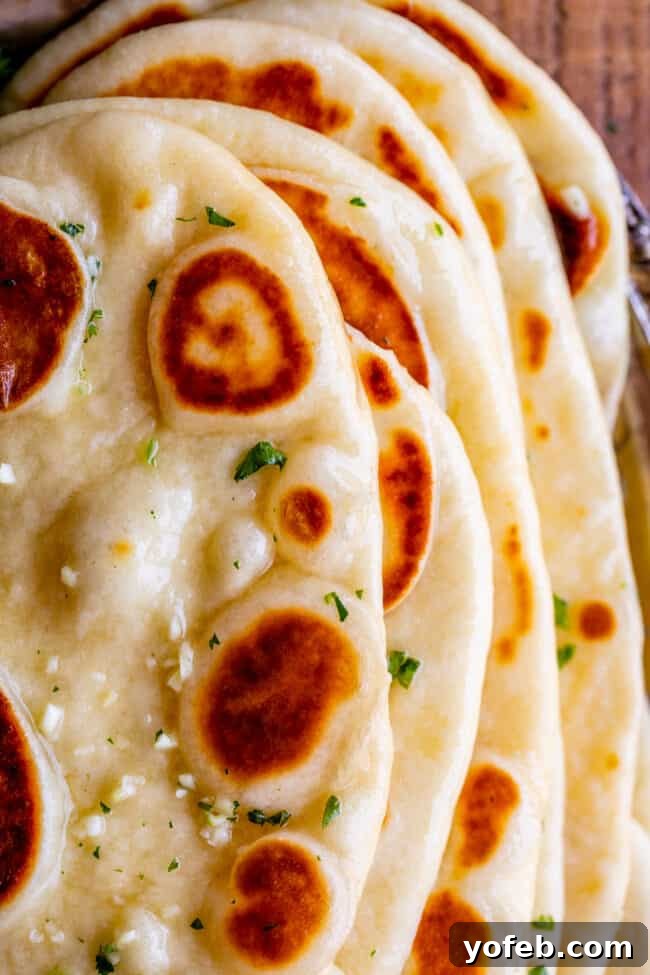 buttered homemade naan with garlic and fresh parsley stacked up, shot from above.