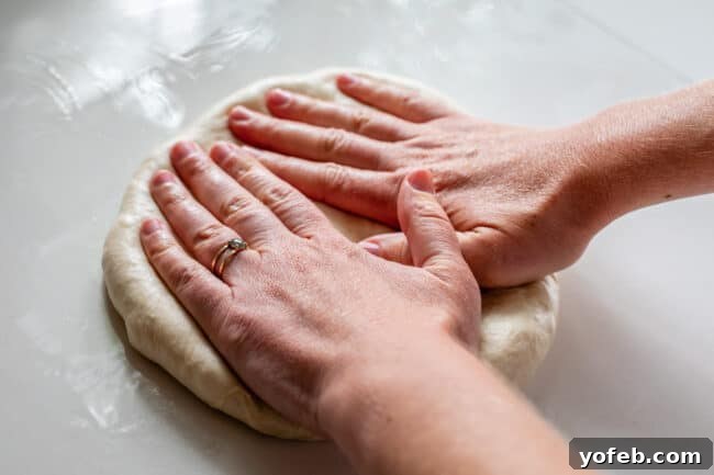 The Ultimate Homemade Pizza Ready When You Are 11 Two hands gently pressing and shaping a ball of pizza dough on an oiled counter.
