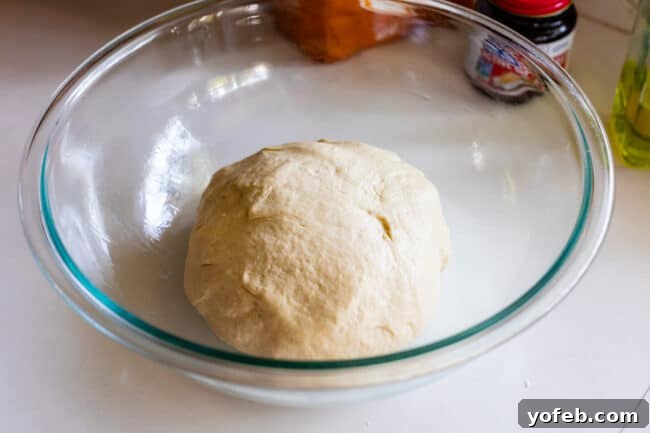 The Ultimate Homemade Pizza Ready When You Are 9 A ball of prepared pizza dough resting in a clear glass bowl on a kitchen counter.