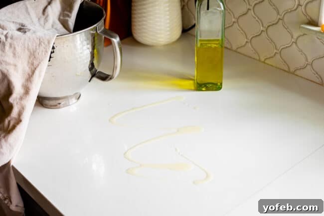 The Ultimate Homemade Pizza Ready When You Are 10 Olive oil drizzled on a white countertop, preparing the surface for rolling out pizza dough.