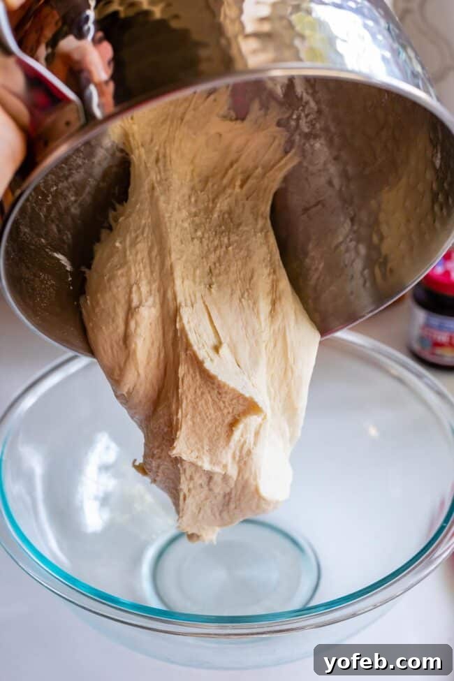Foolproof Pizza Dough for Newbies 17 pouring a homemade pizza dough recipe from a stand mixer into a glass bowl.
