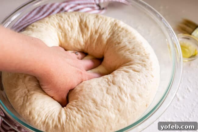 Foolproof Pizza Dough for Newbies 19 punching down pizza dough in a glass bowl.
