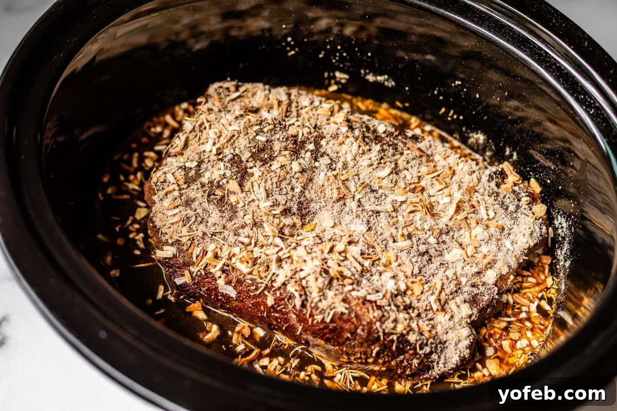 Ultimate Slow Cooker French Dip Sandwiches 13 A seasoned chuck roast, generously coated with dried onion soup mix and herbs, rests in a slow cooker, submerged in a rich, savory broth, awaiting the slow cooking process that will transform it into tender perfection.