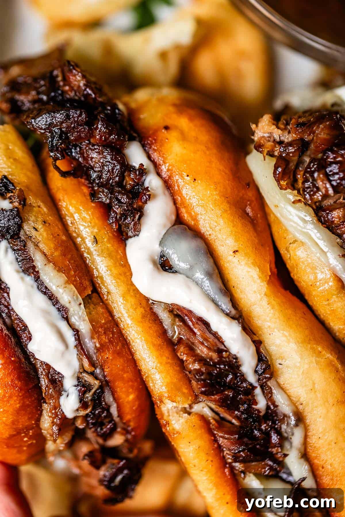 Ultimate Slow Cooker French Dip Sandwiches 6 Close-up of a toasted sandwich filled with shredded beef, melted provolone cheese, and a creamy white horseradish sauce. The golden-brown bread is slightly glossy, showcasing the tender meat and gooey cheese inside.