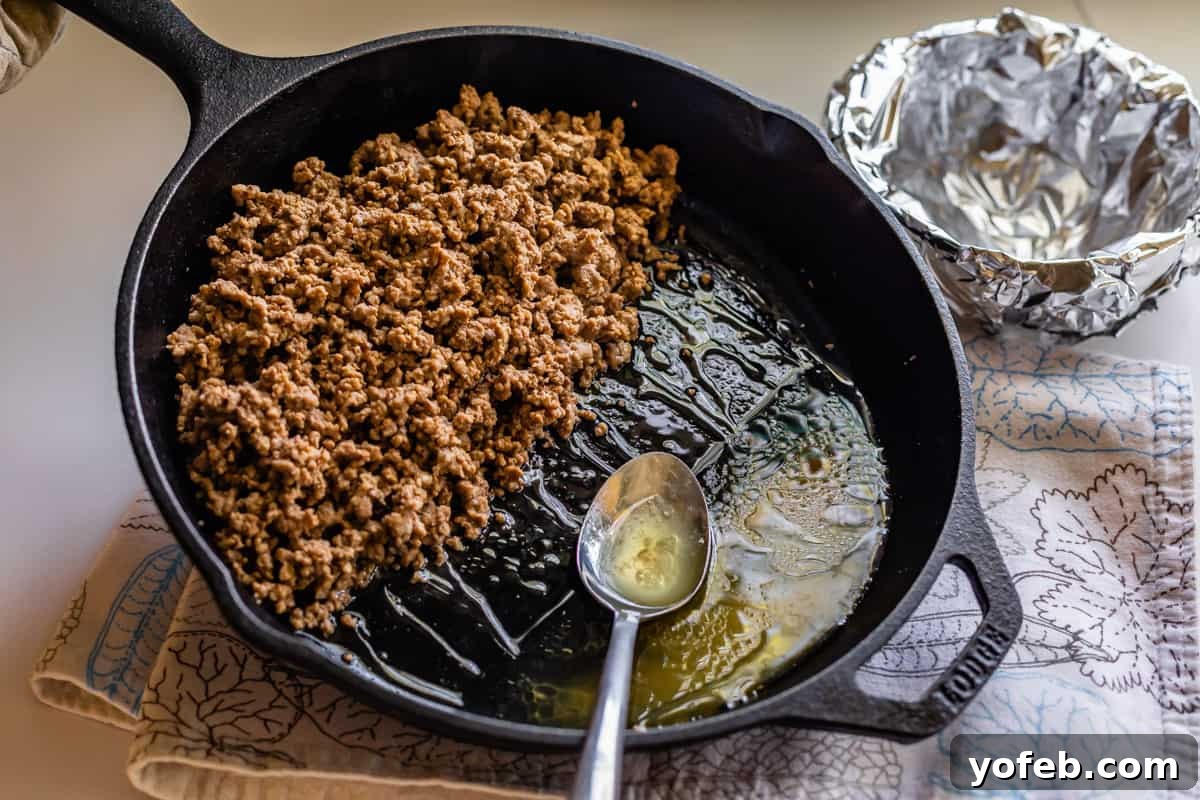 Elevate Your Tacos with Homemade Seasoning 11 A cast iron skillet of cooked ground beef with grease being drained into a foil-lined bowl.