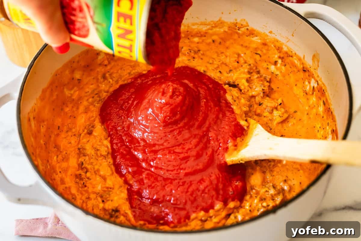 The Definitive Lasagna Soup 14 A hand pouring crushed tomatoes from a can into a large soup pot with the savory mixture.